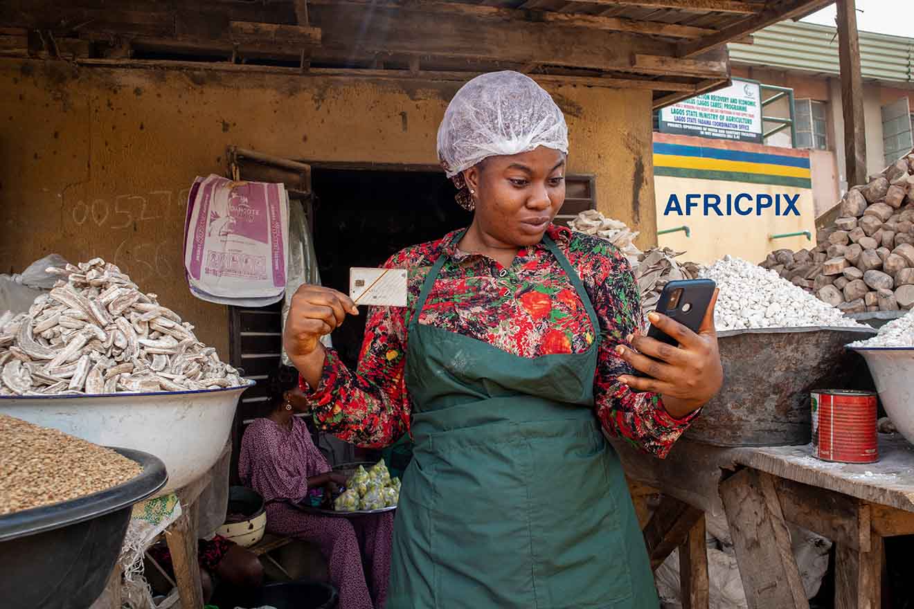 Happy African Woman Holding ATM Card and Phone in Front of Her Shop